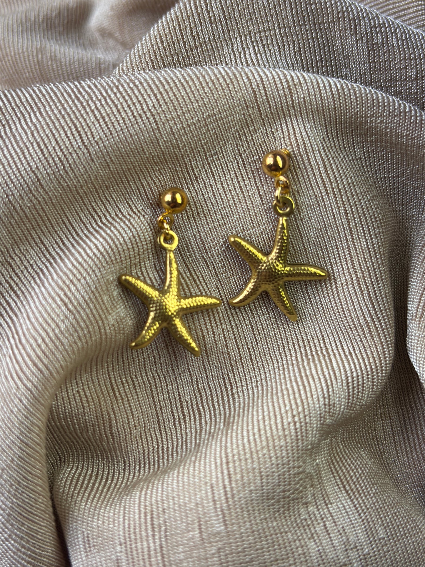 golden sea stars earrings flat on a beige fabric