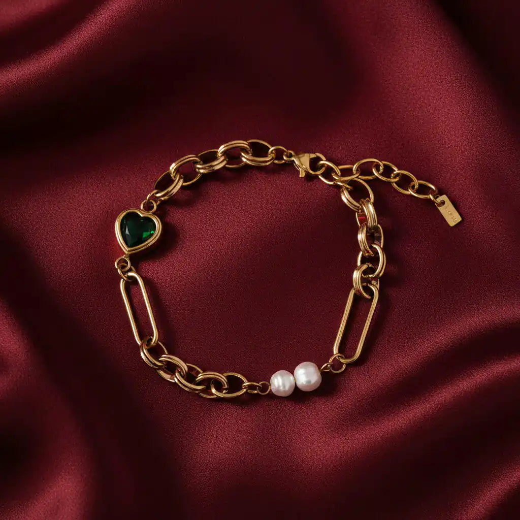 Gold chain bracelet with a heart-shaped green gemstone and pearl on a white background